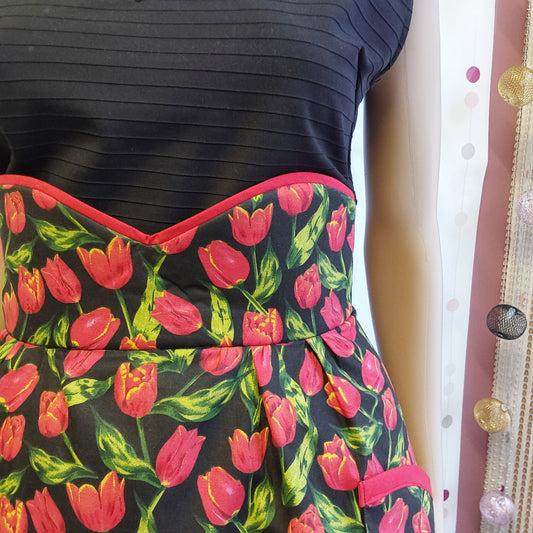 Half apron in black cotton and red tulips print, close up of a high waist with red piping in the top