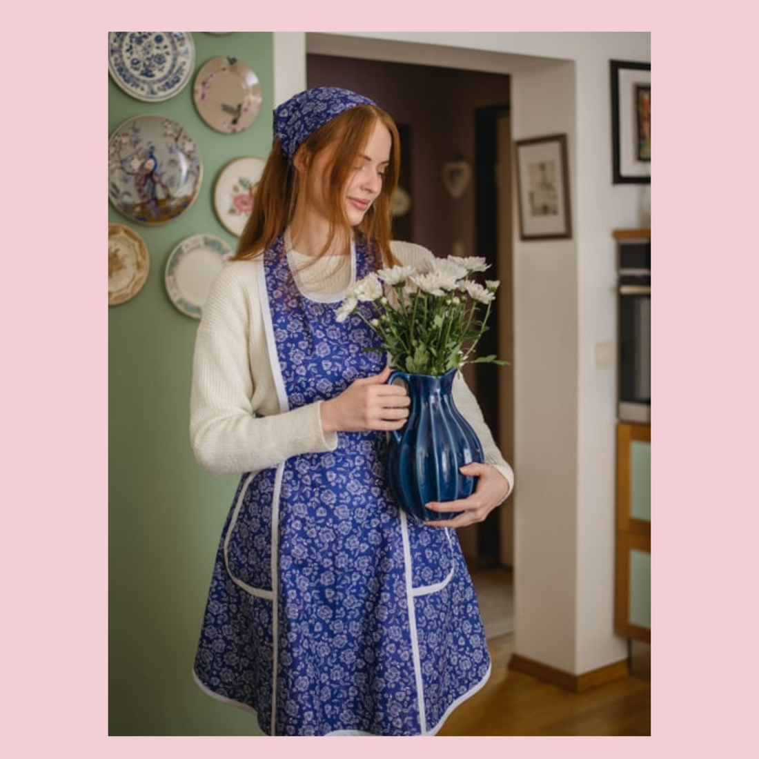 women in dressed in blue retro apron, carryin a vase with white flowersg