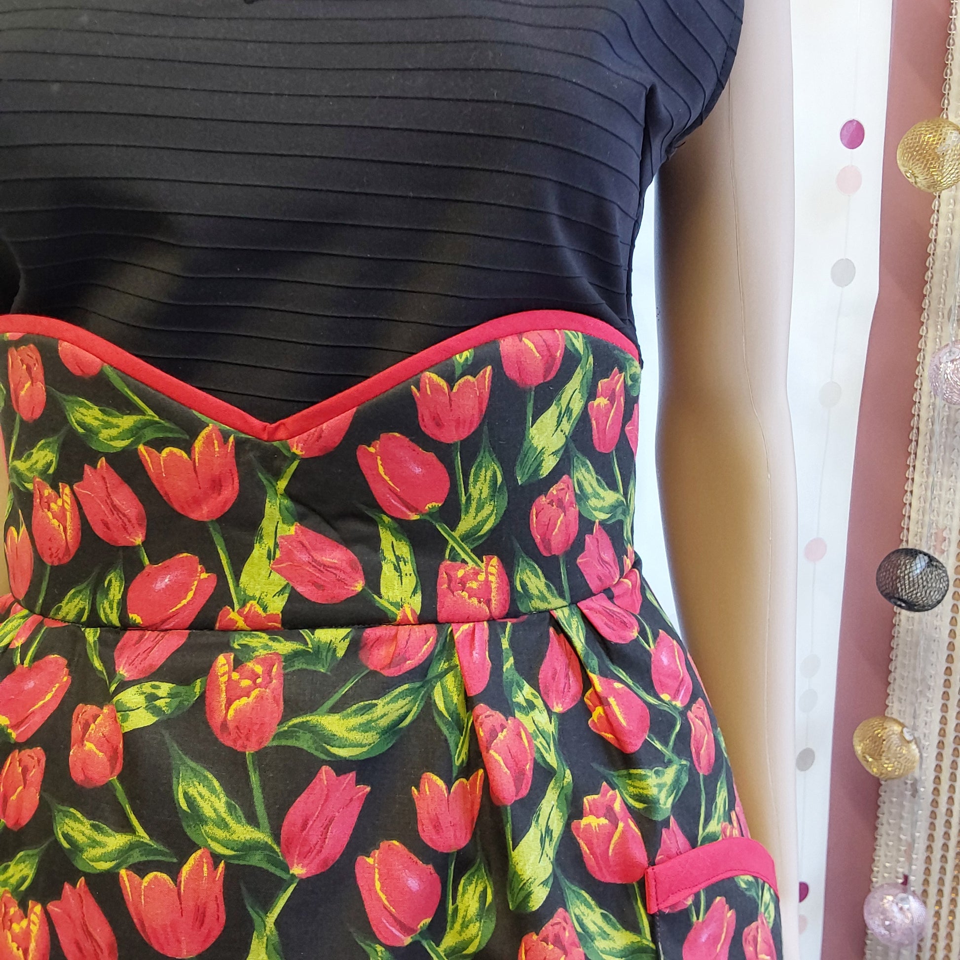 Half apron in black cotton and red tulips print, close up of a high waist with red piping in the top
