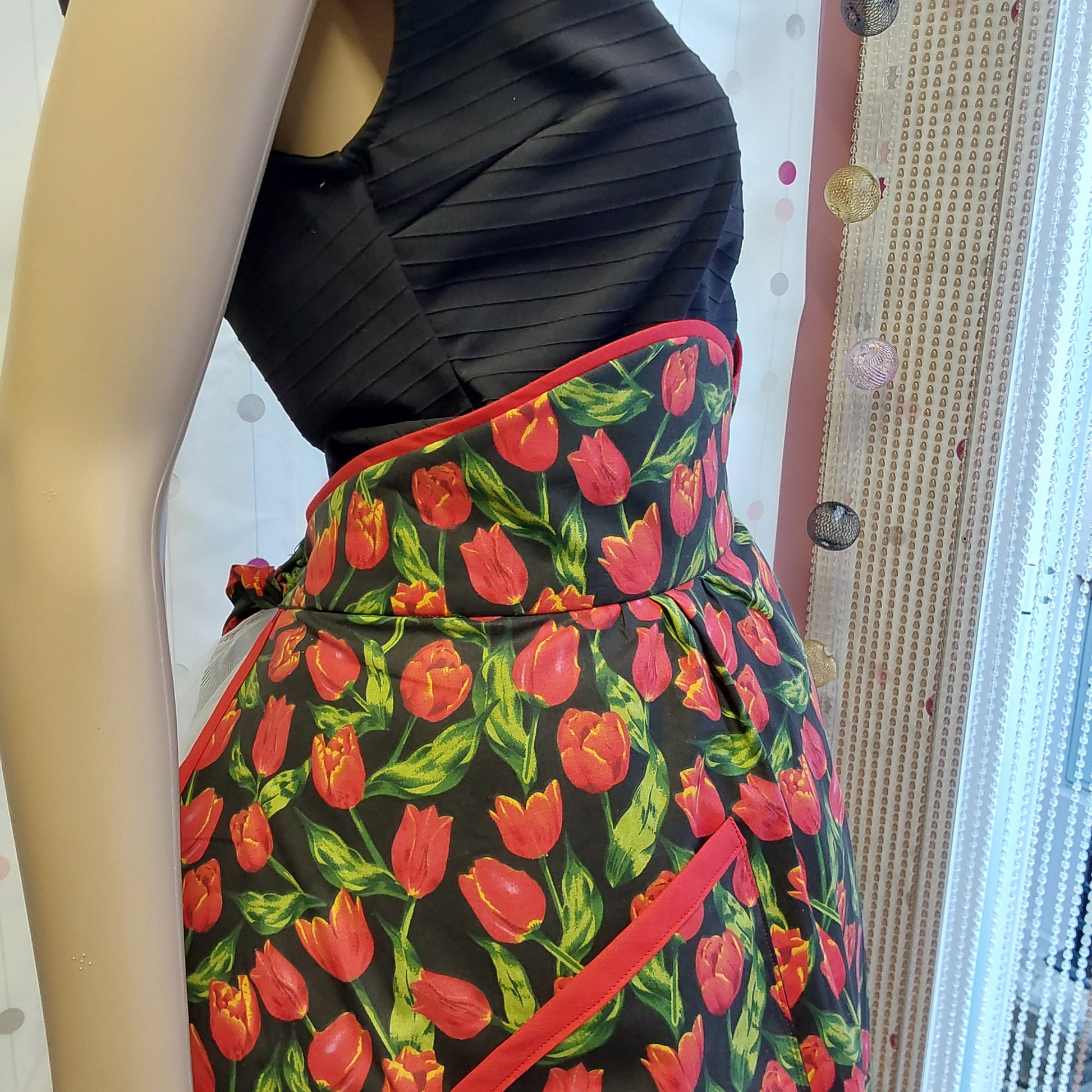close up photo of a side of a half apron with high waist, black cotton with red tulips print, red bias trimming 