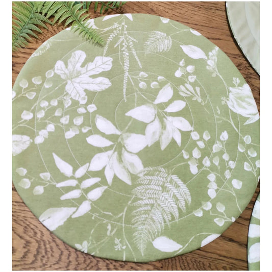 A round quilted placemat, soft green colour,white botanical print on it