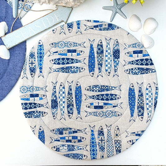 A round quilted placemat with a beige background and a blue sardines fish print