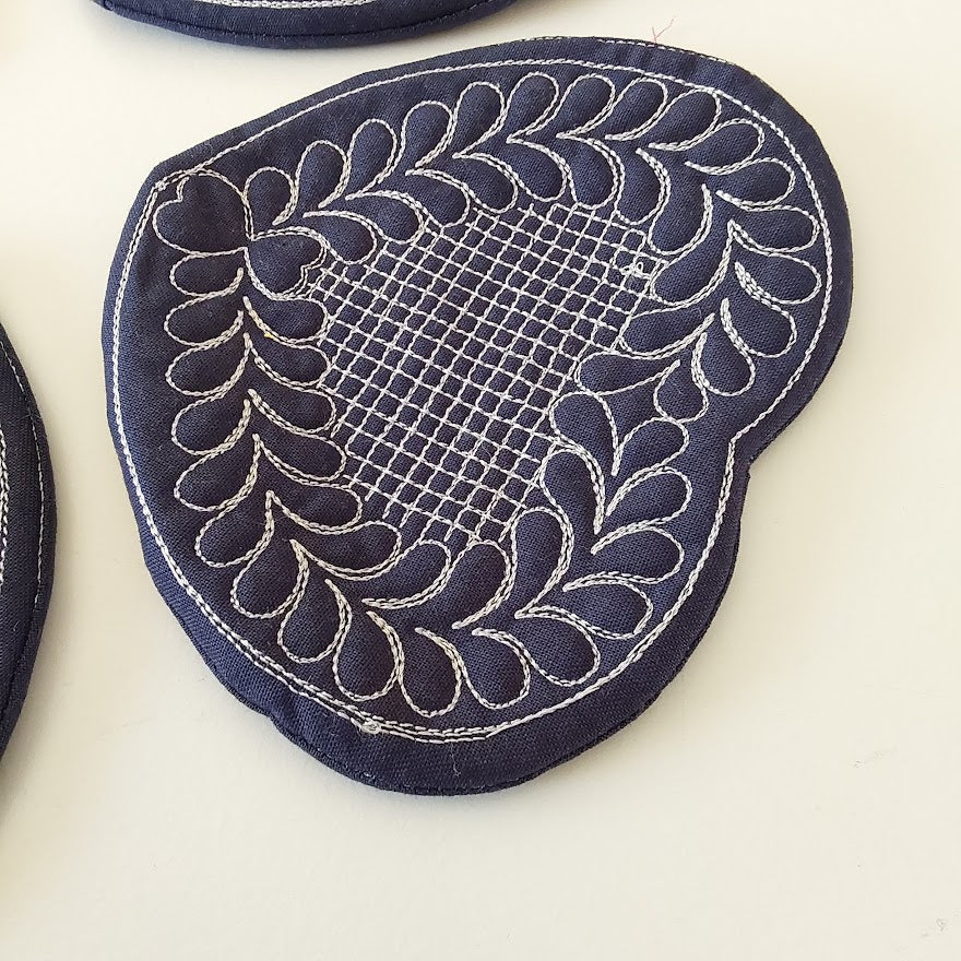 Navy blue fabric patch with intricate white embroidery on a light beige background