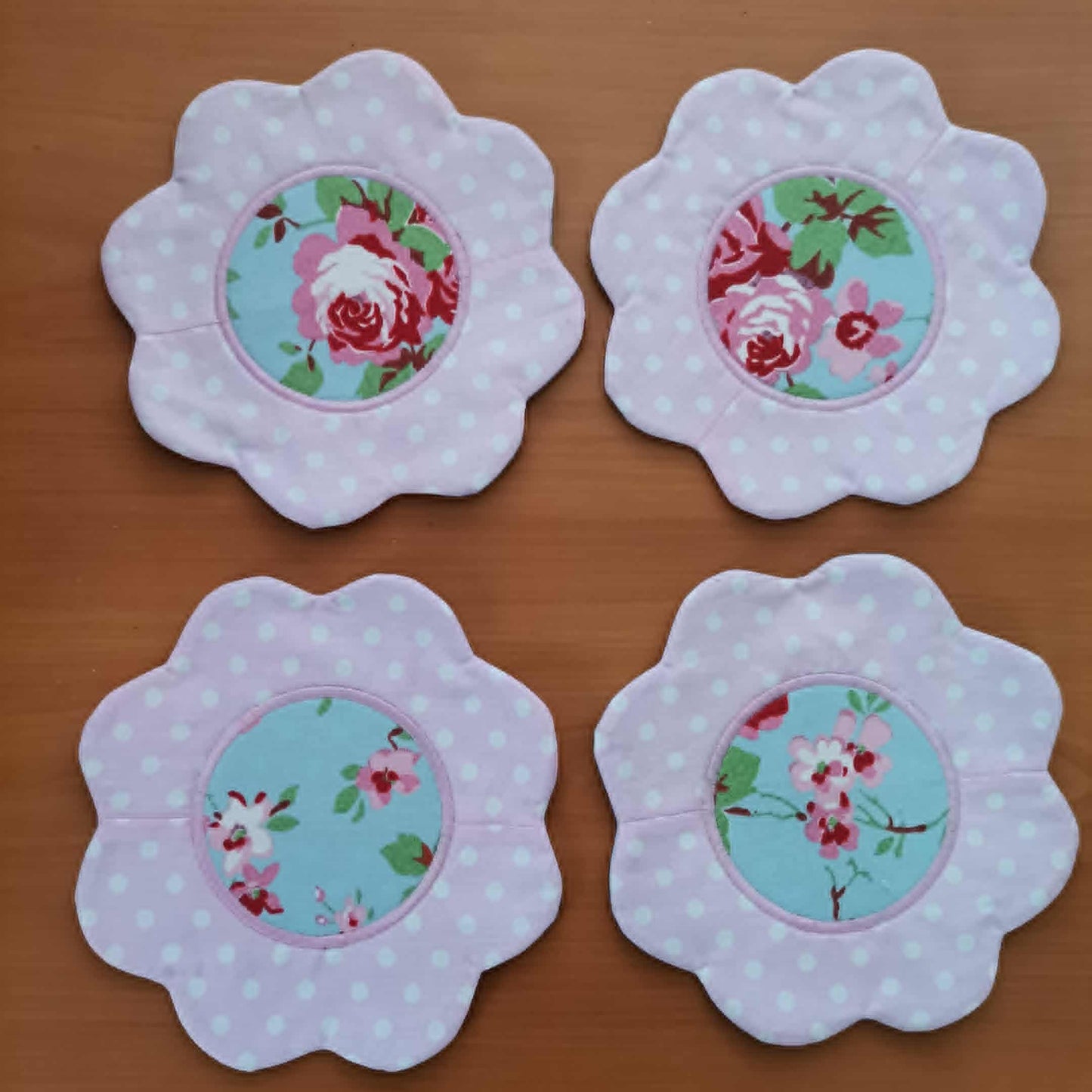 Four floral coasters with polka dot borders on a wooden surface