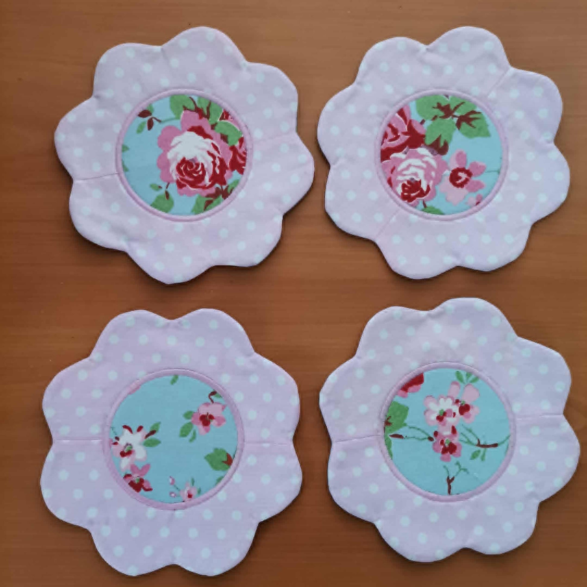 Four floral coasters with polka dot borders on a wooden surface