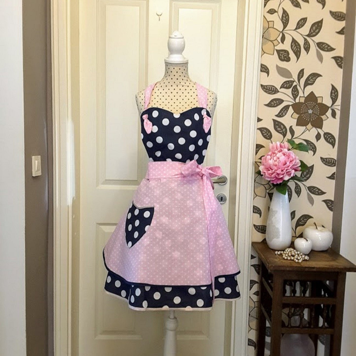 A flirty apron in retro style with a polka dot pattern. The apron is primarily navy blue with a skirt in pink polka dots and blue pocket, apron has a pink bow at the waist,  apron Sophia is handmade in Slovenia