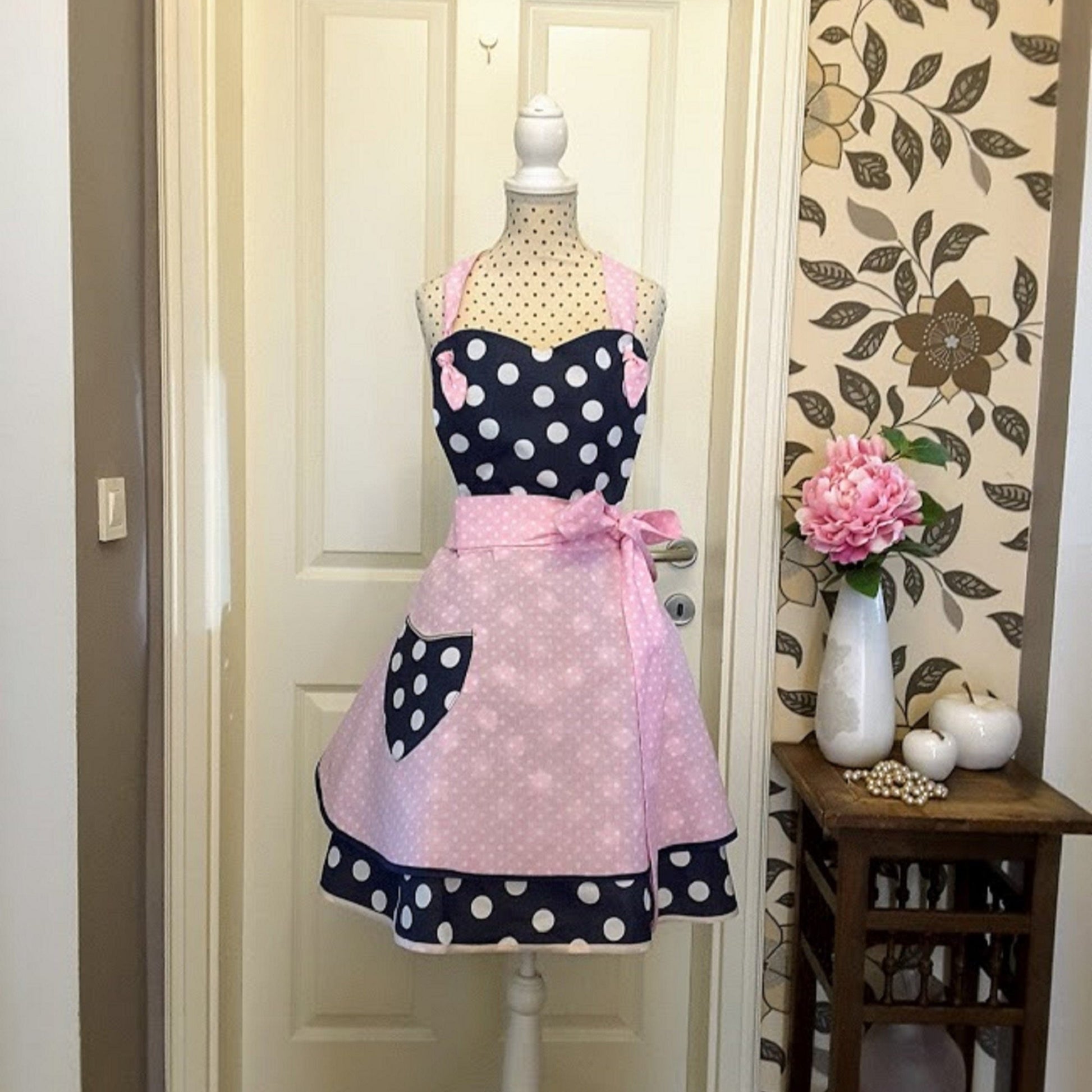 A flirty apron in retro style with a polka dot pattern. The apron is primarily navy blue with a skirt in pink polka dots and blue pocket, apron has a pink bow at the waist,  apron Sophia is handmade in Slovenia