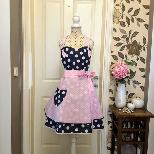 A flirty apron in retro style with a polka dot pattern. The apron is primarily navy blue with a skirt in pink polka dots and blue pocket, apron has a pink bow at the waist,  apron Sophia is handmade in Slovenia